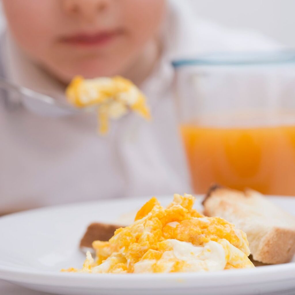 little boy eating scrambed eggs and a glass or orange juice